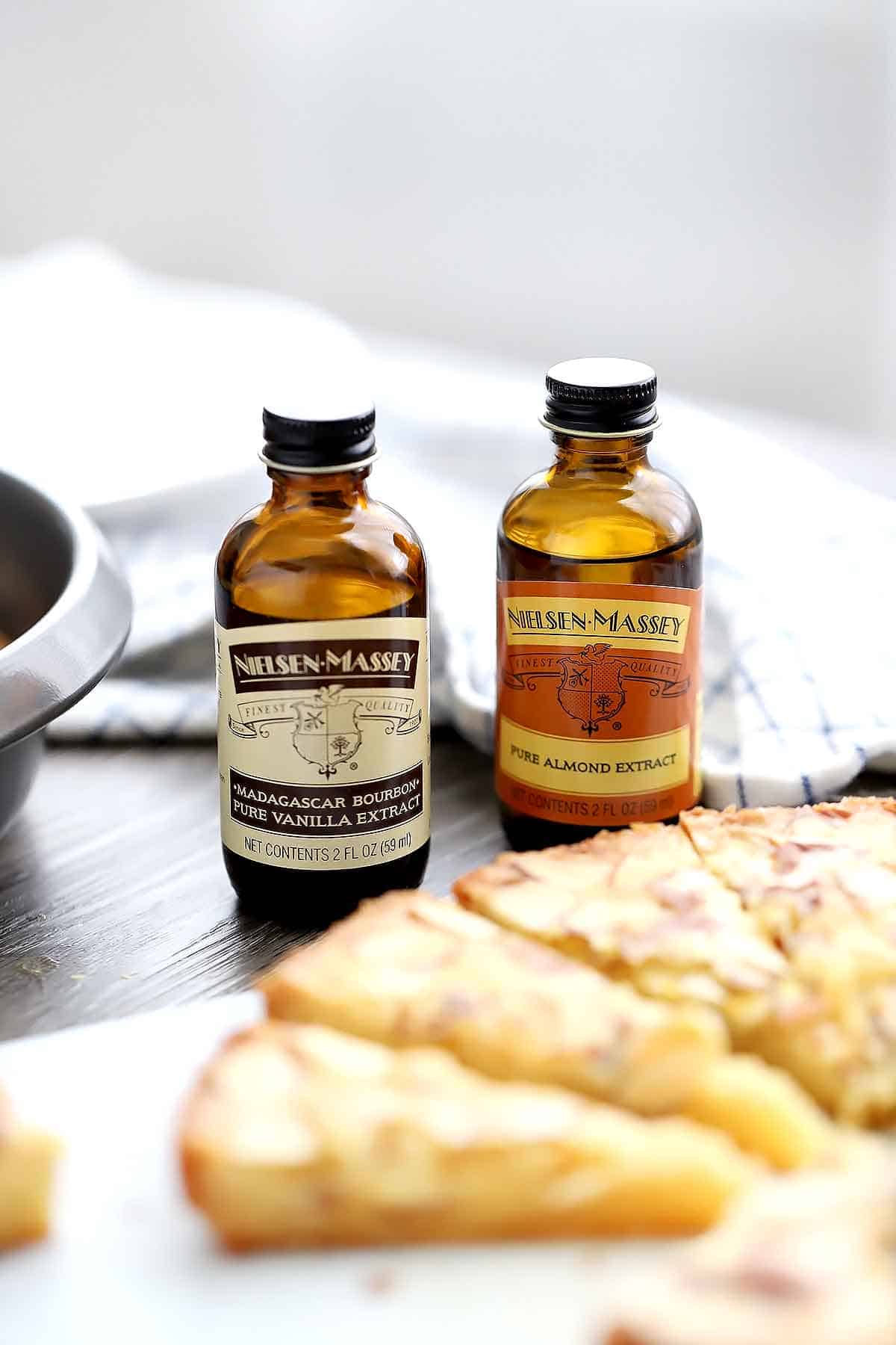 Bottles of Nielsen-Massey Pure Almond Extract and Madagascar Bourbon Vanilla Extract with a butter cake.