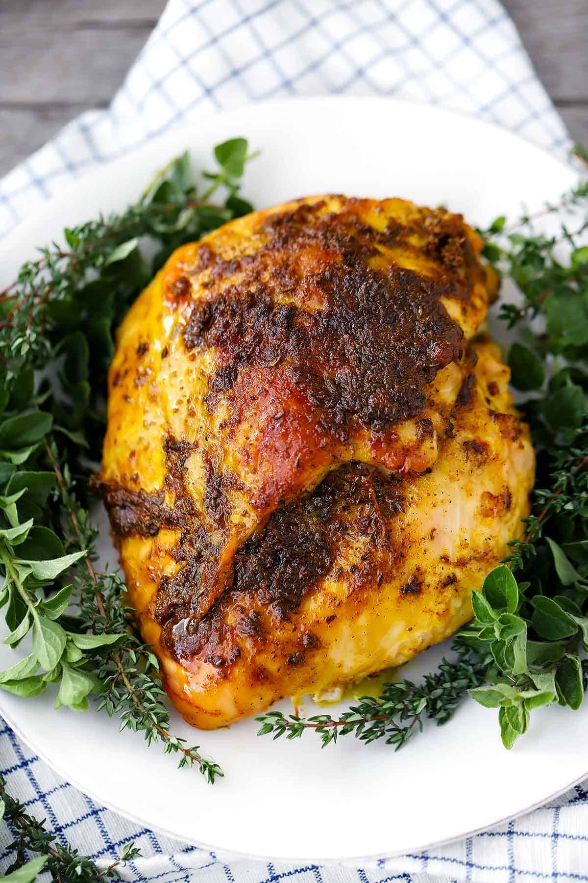 A boneless turkey breast on a white plate with herbs around it.