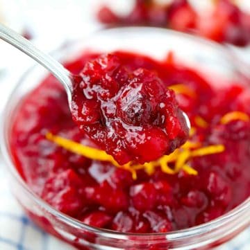 A spoonful of spiced orange cranberry sauce over a bowl with orange zest on top.