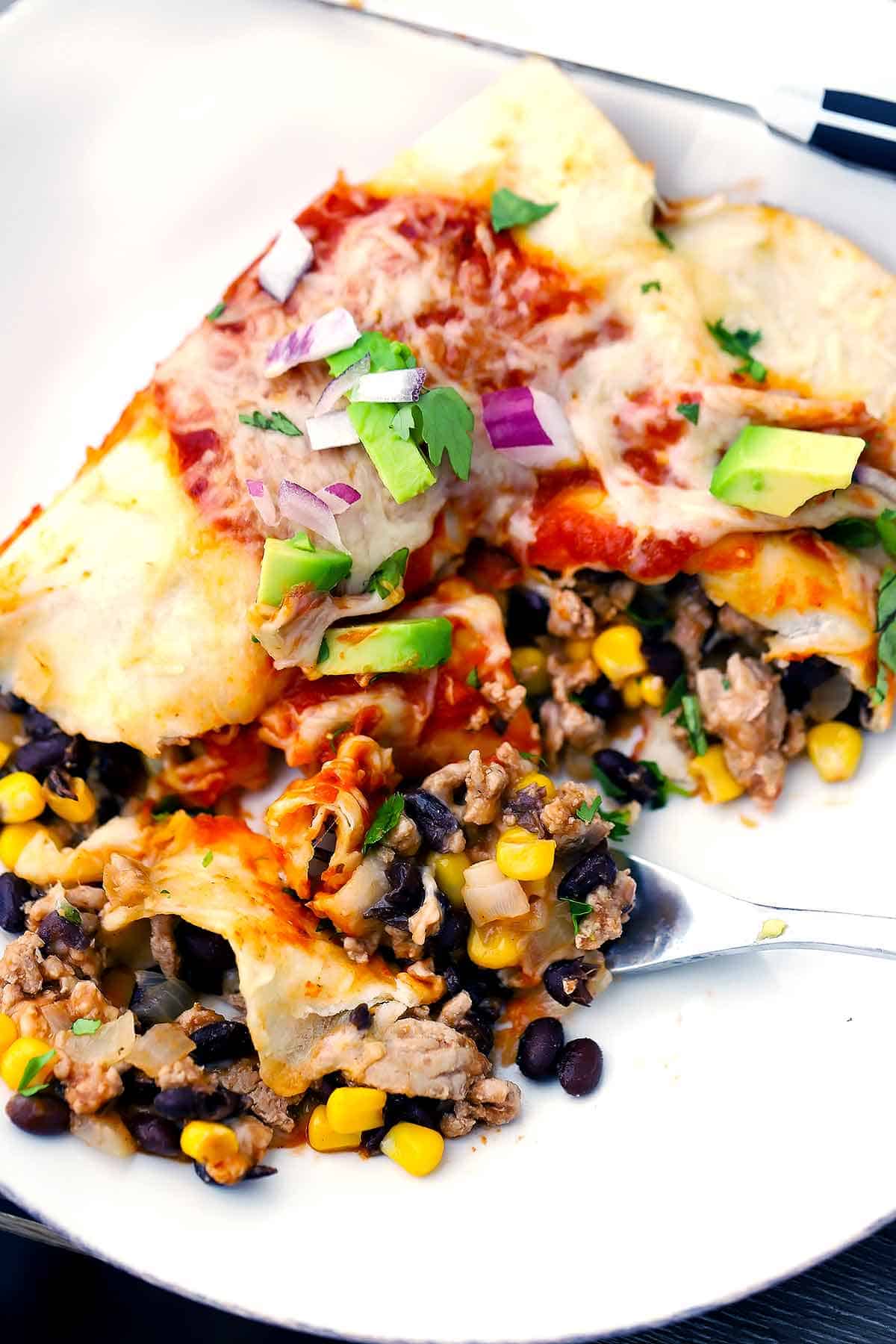 Turkey enchiladas cut in half on a white plate with black beans and corn.