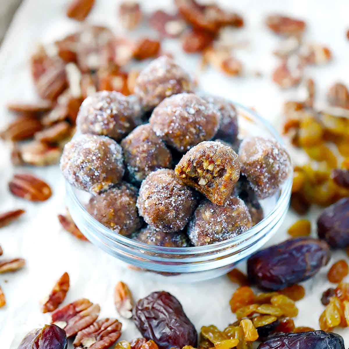 A bowl filled with gingerbread energy balls with pecans, dates, and raisins scattered around it.