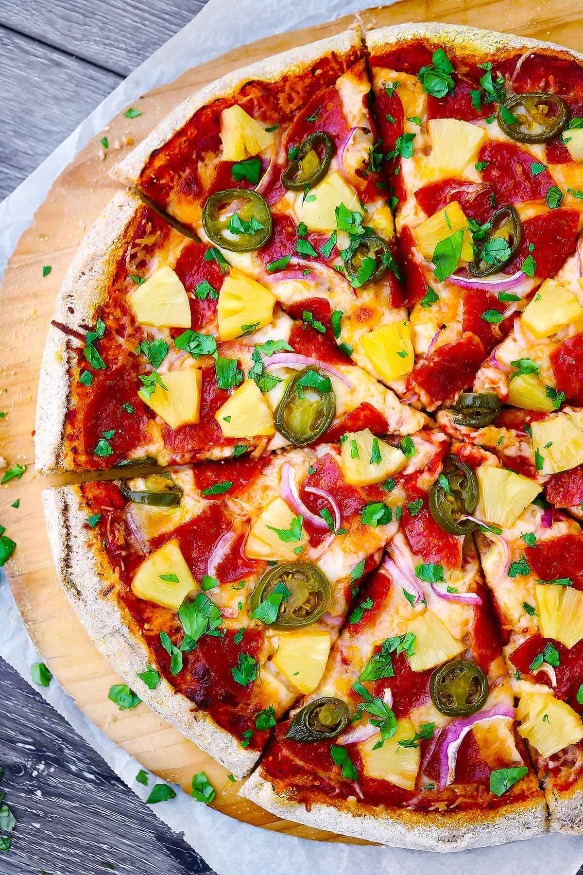 Overhead photo of sliced hawaiian pizza sprinkled with fresh cilantro.