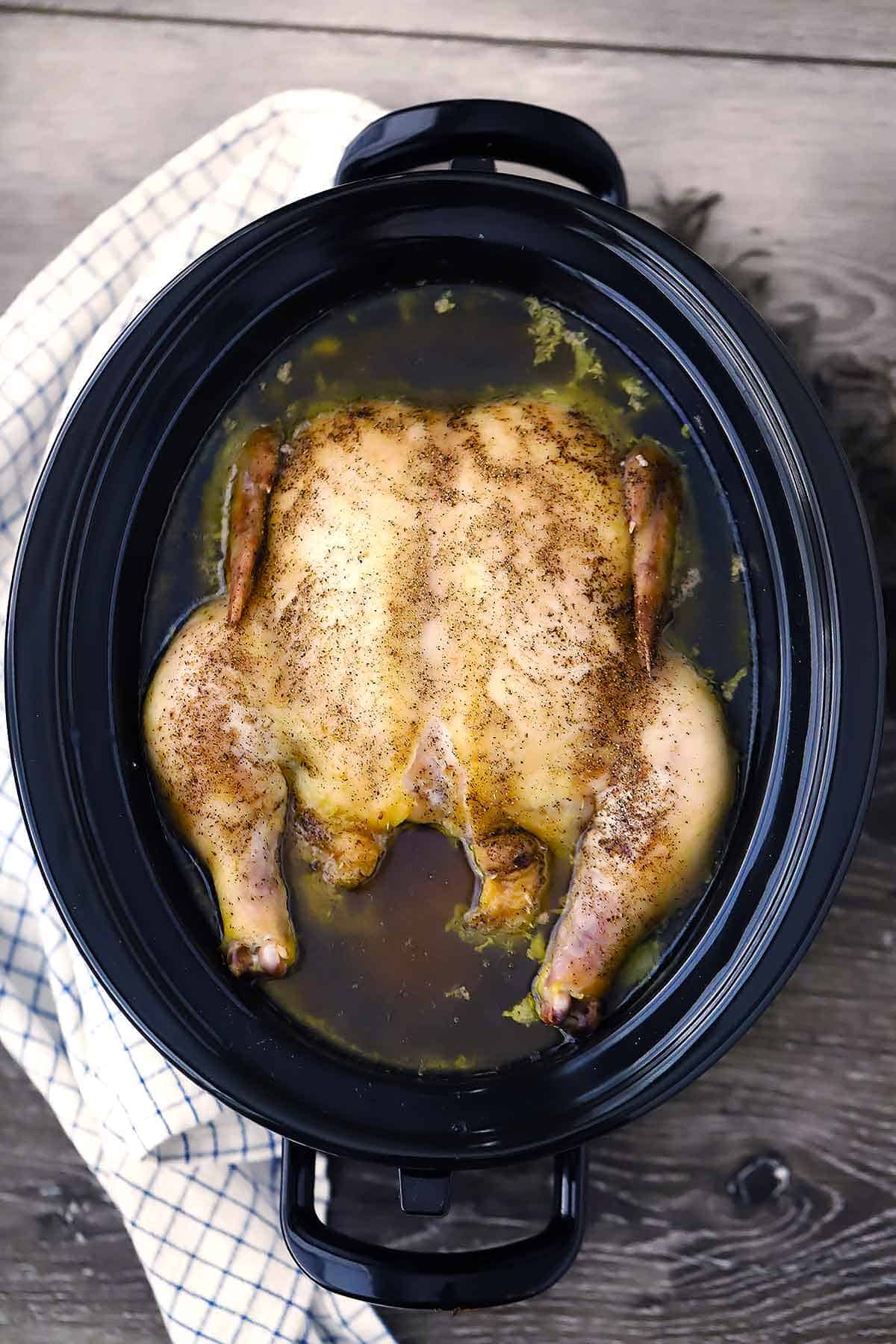 A slow cooker with a whole chicken and chicken stock in it.