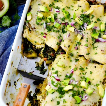 A white baking dish with vegetarian enchiladas verdes topped with avocado and onion