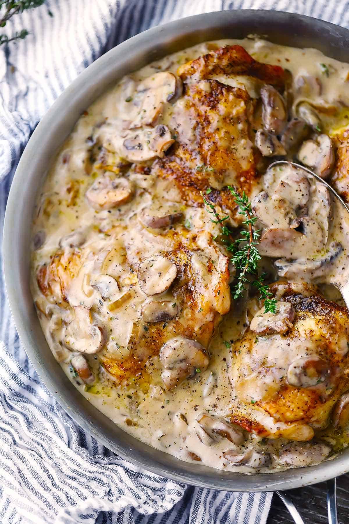 Roasted chicken thighs in creamy mushroom sauce with sprigs of thyme in a skillet.
