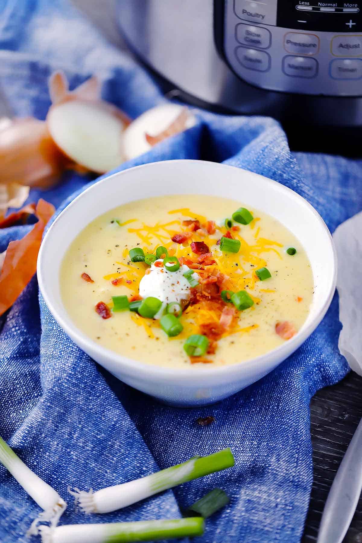 A bowl of baked potato soup with an instant pot in the background on a blue towel.
