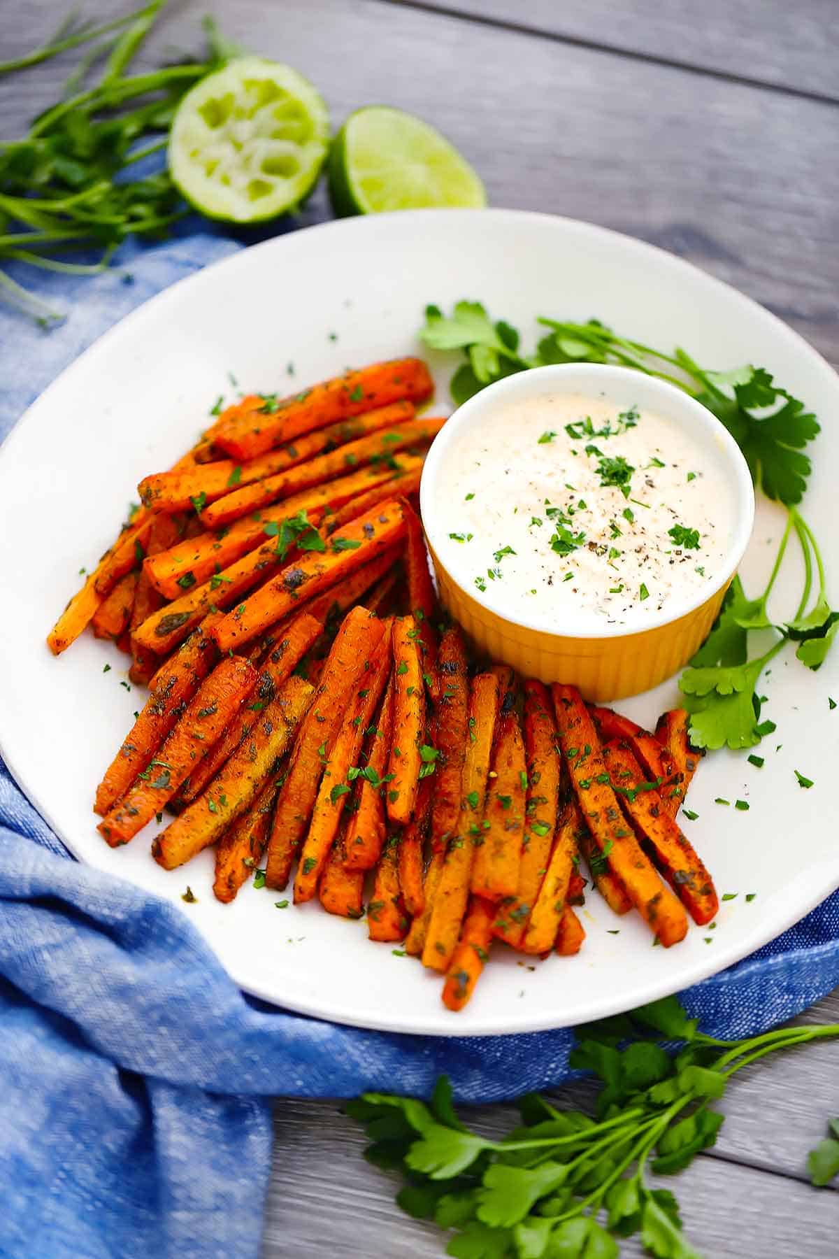 Carrot fries on a plate sprinkled with parsley and dipping sauce.