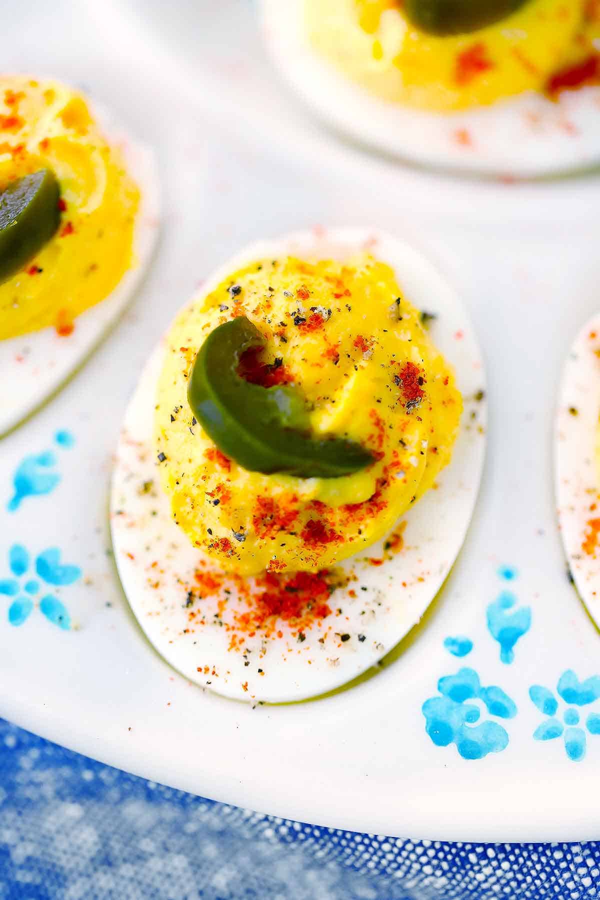 Close up photo of a deviled egg with a jalapeño pepper on top.