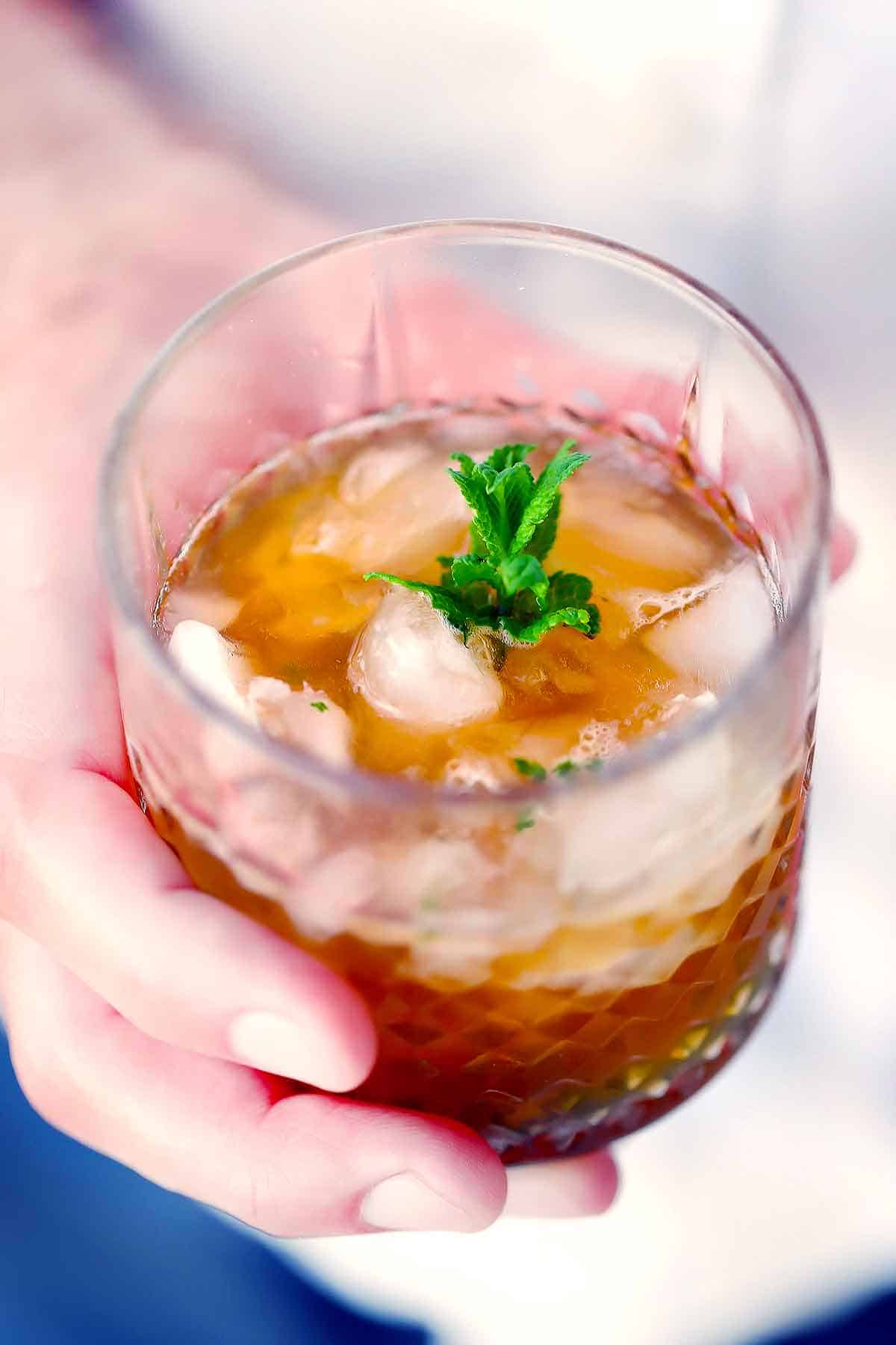 A mint julep whiskey cocktail with fresh mint being held.