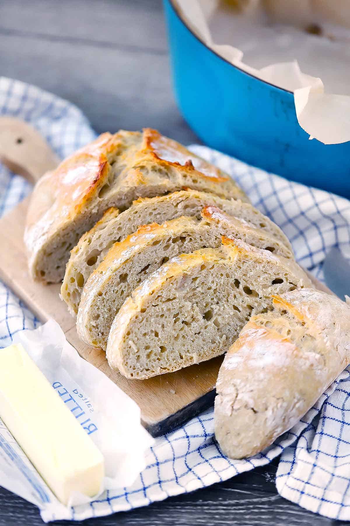 Homemade no knead bread sliced with Dutch oven behind it.