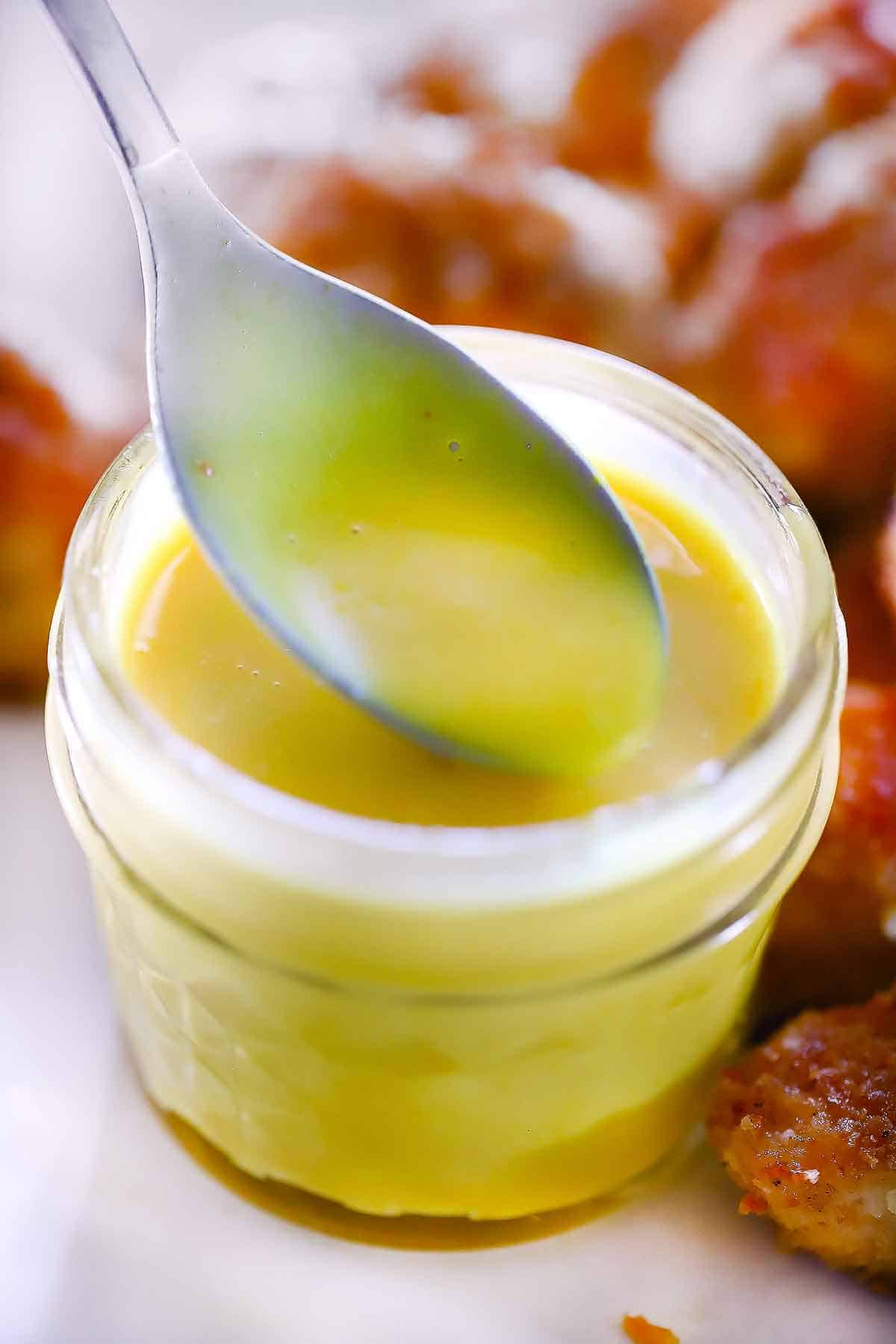 Homemade honey mustard dressing in a jar with a spoon.