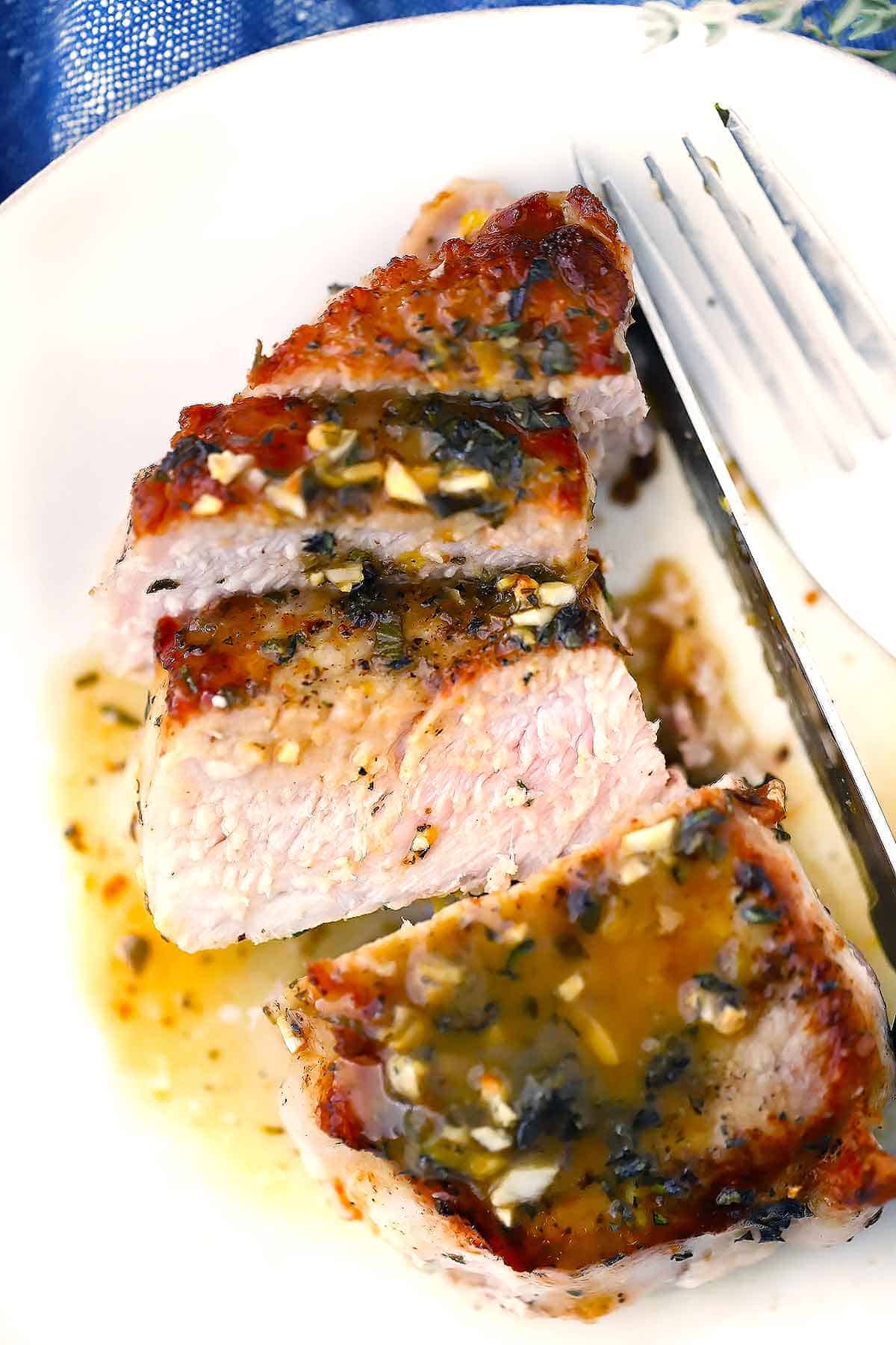 An oven baked pork chop sliced on a plate with pan sauce.
