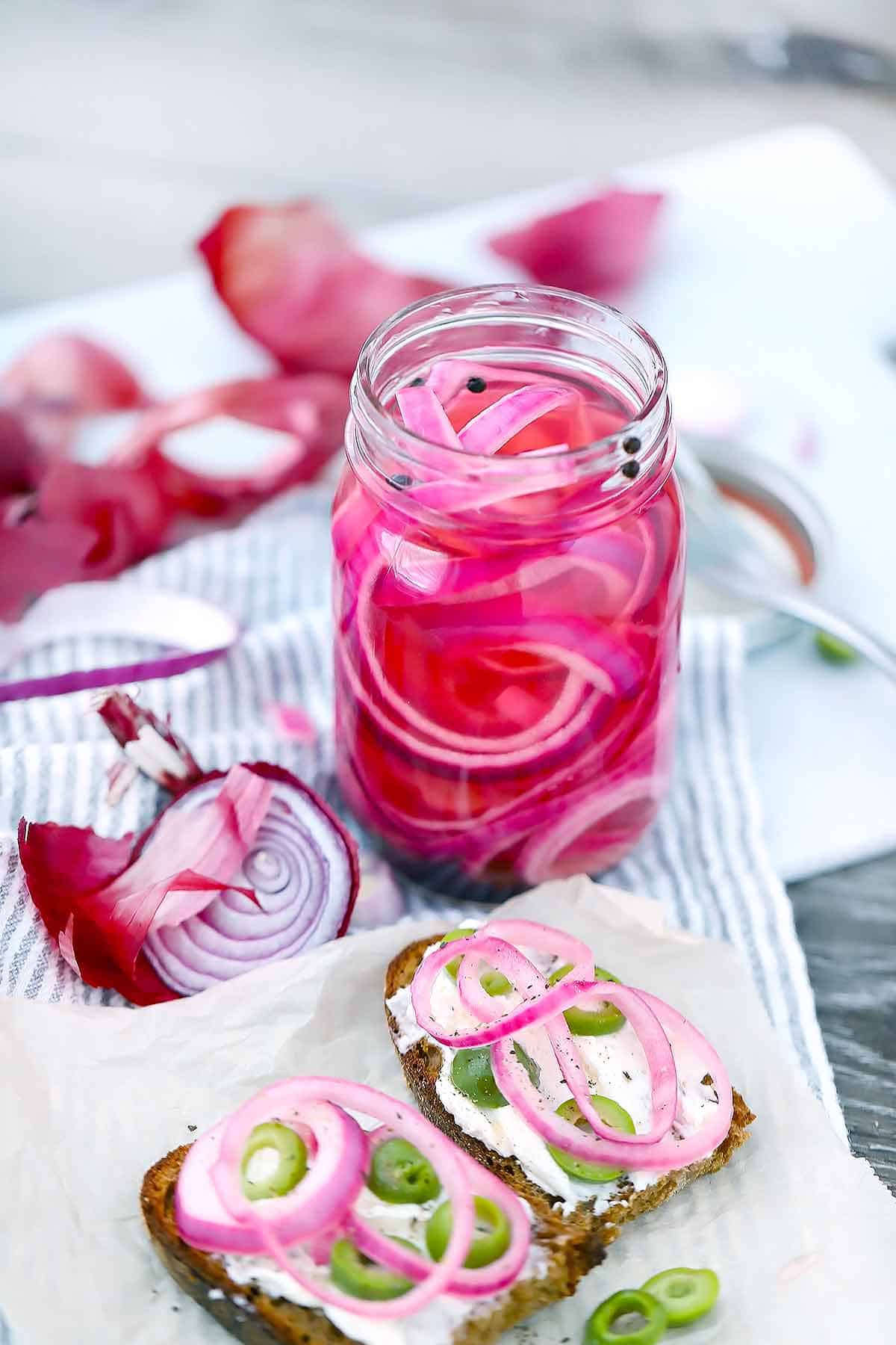 Pickled red onions in a jar with toast and cream cheese and olives.