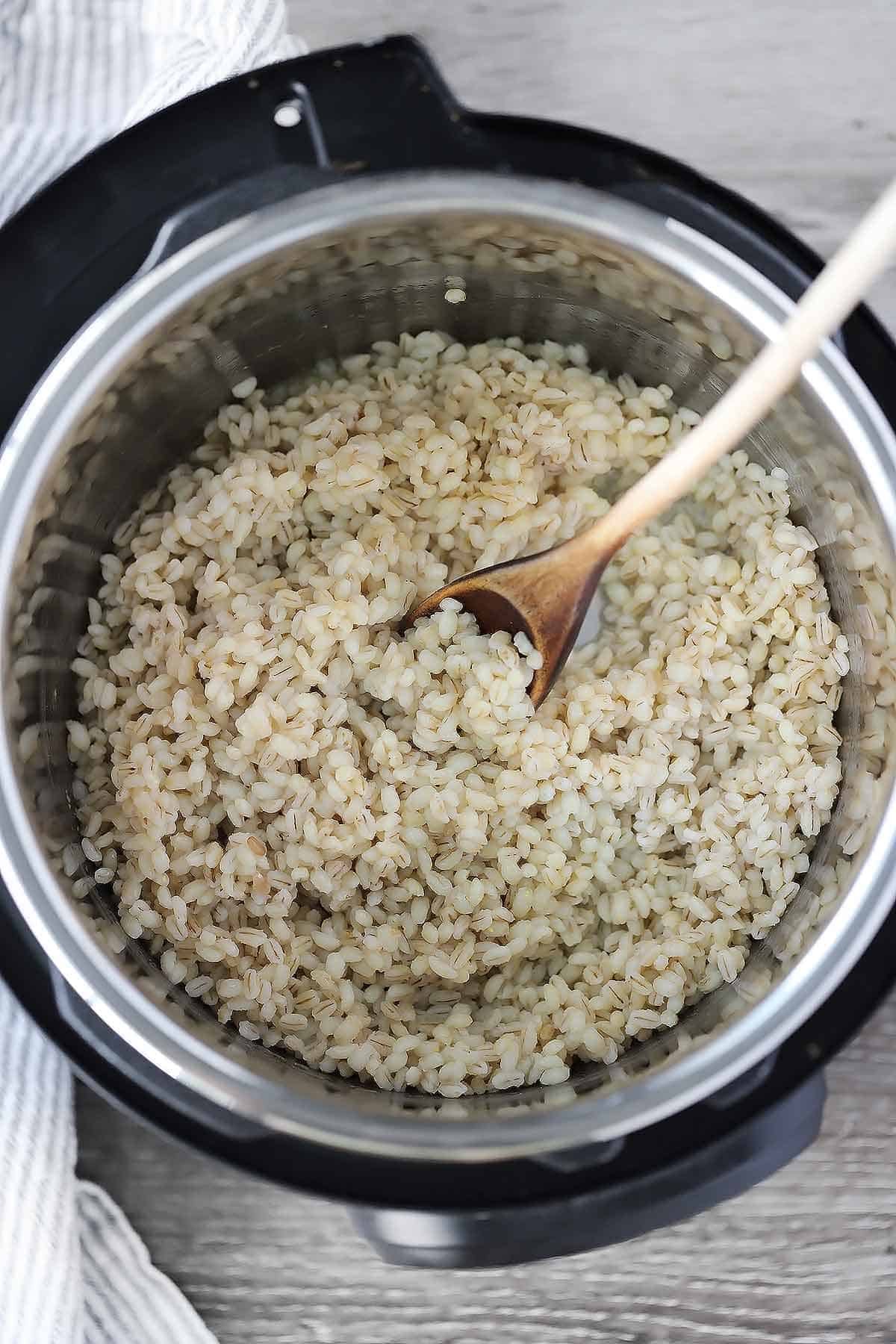 Cooked barley in an instant pot with a wooden spoon.