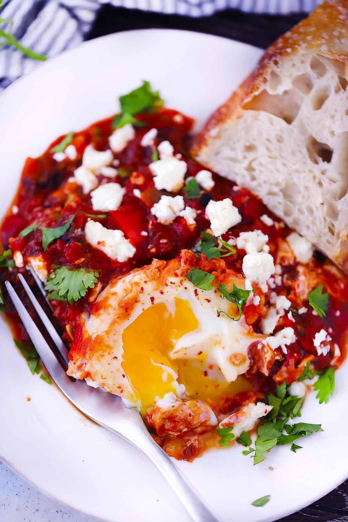 A plate with shakshuka and a runny yolk egg with a piece of bread.