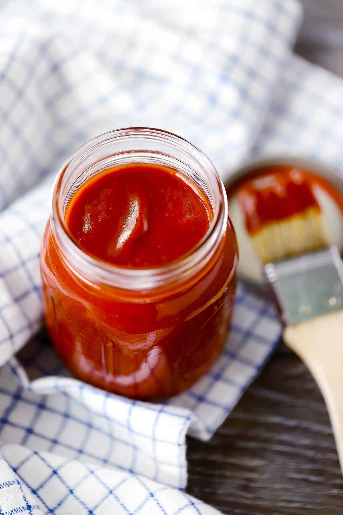 A mason jar of barbecue sauce with a basting brush on the side.