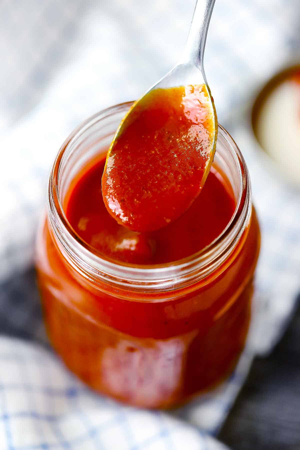 A jar of homemade barbecue sauce with a spoonful hovering above.