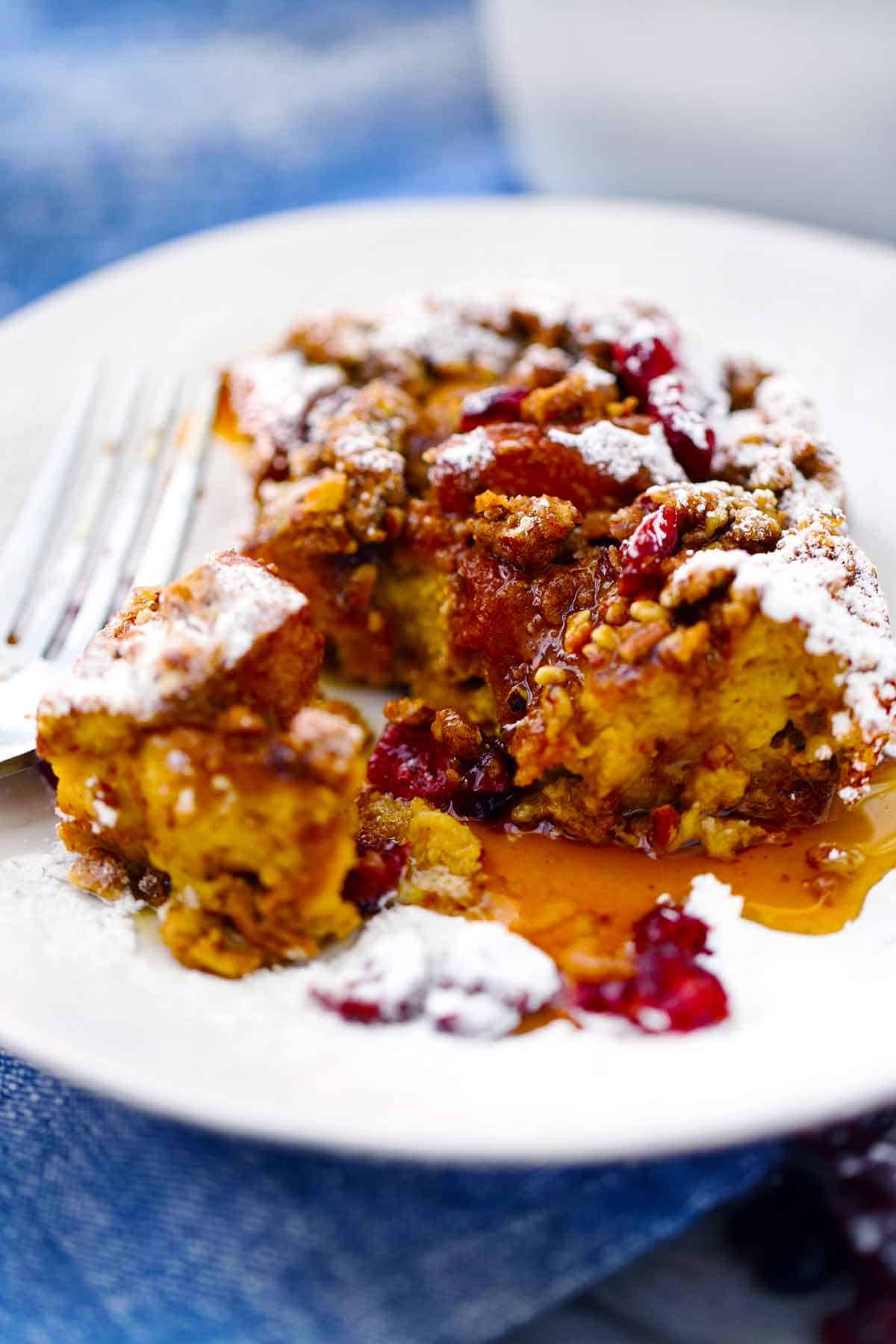 Pumpkin french toast casserole on a plate with powdered sugar and maple syrup.