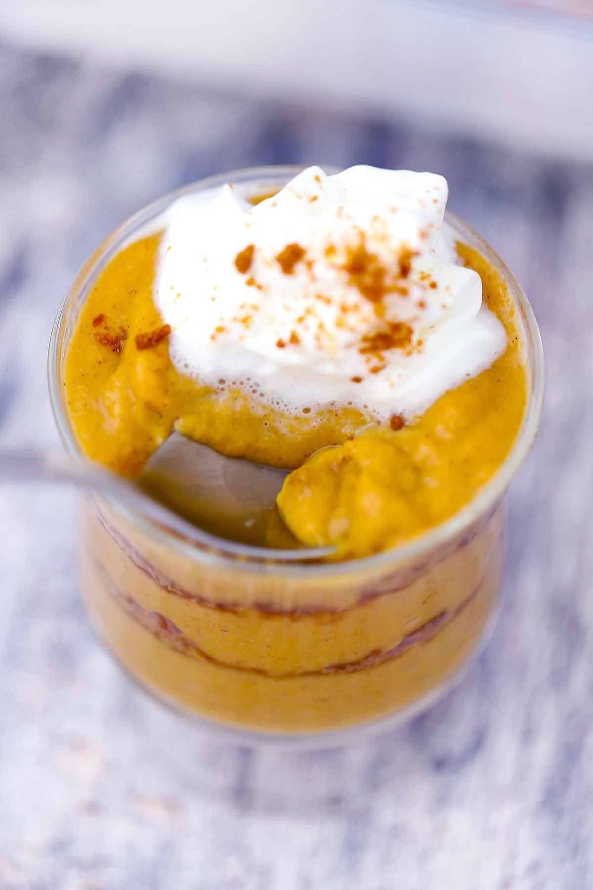 A spoon taking a scoop of pumpkin pudding out of a dessert glass.