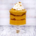 Square photo of pumpkin pudding layered in dessert glass with gingerbread cookie crumbles and whipped cream.