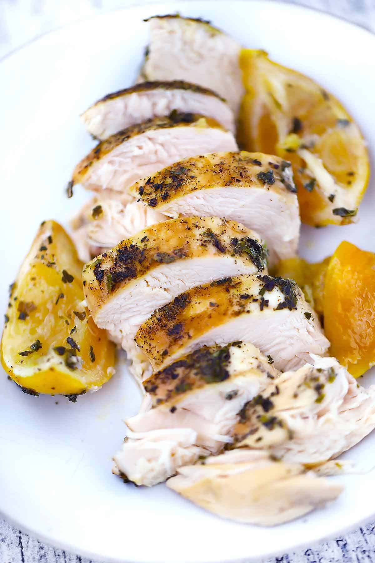 A sliced chicken breast on a white plate with lemon wedges.