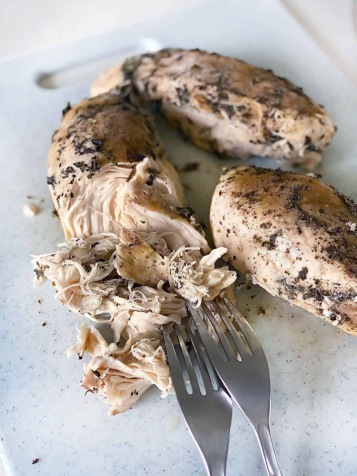 Shredding chicken breasts on a cutting board with two forks.