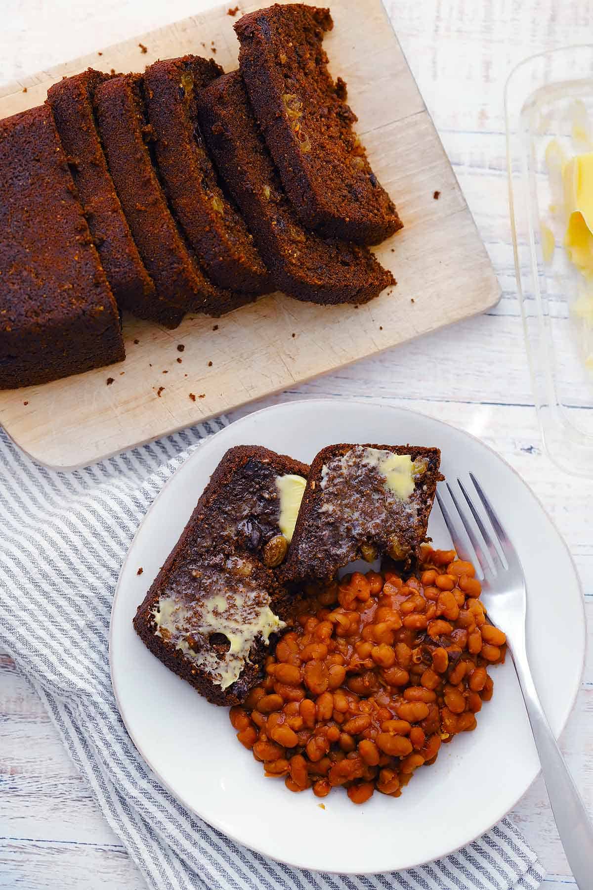 Overhead photo of a sliced loaf of Boston brown bread and a plate with slices and beans.