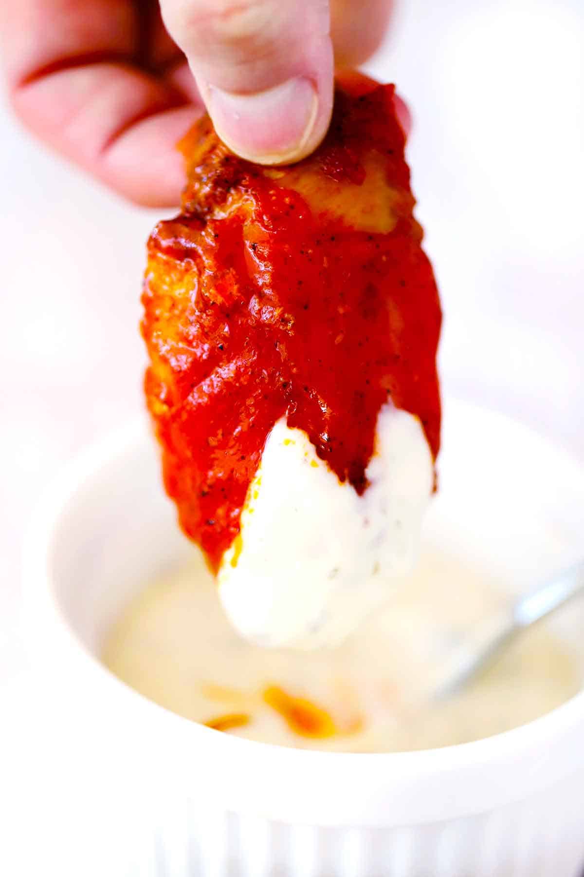A buffalo wing being dipped into ranch dressing.