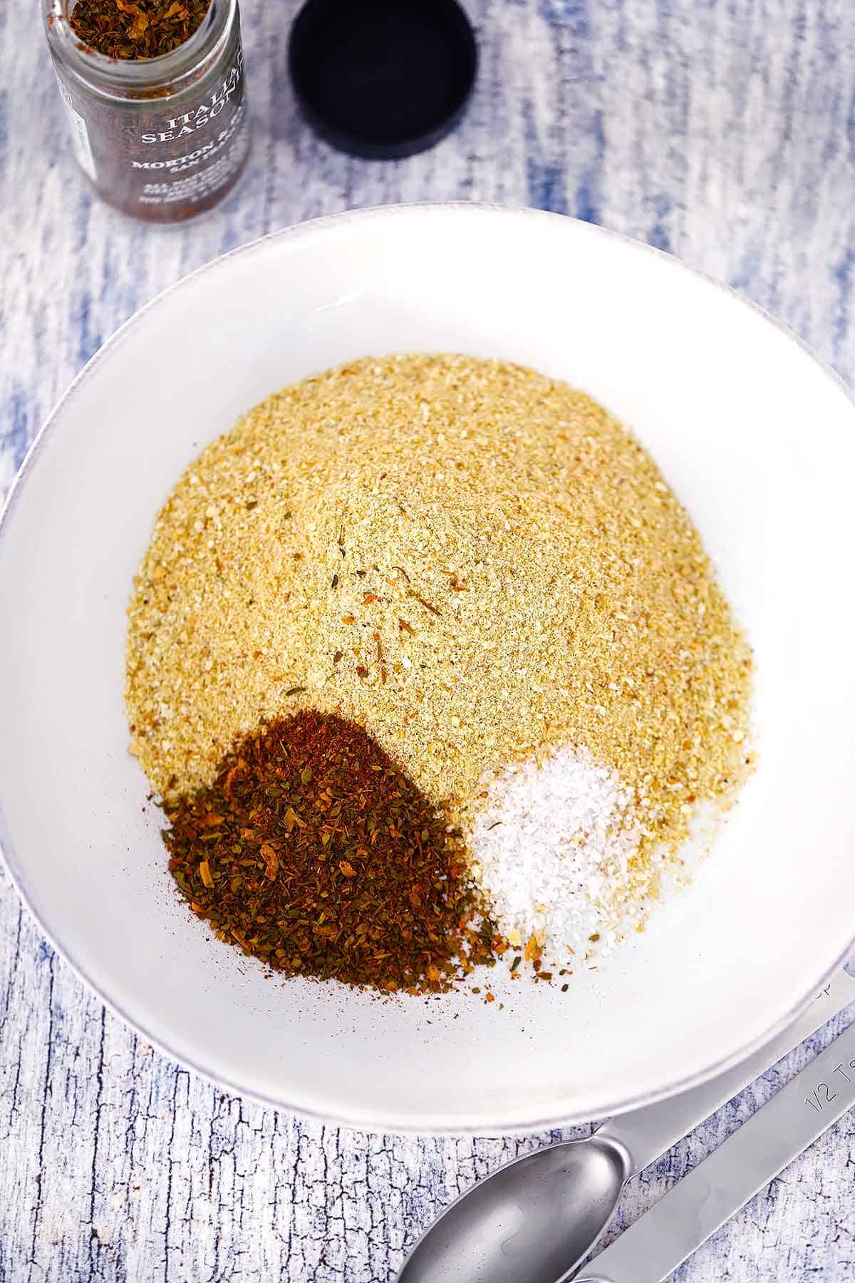 The ingredients for homemade Italian seasoned bread crumbs - plain bread crumbs, Italian seasoning, and salt - in a white bowl.