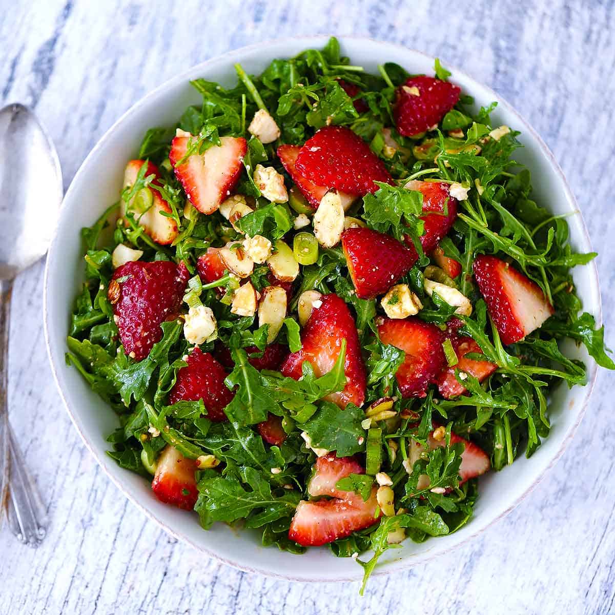 Overhead square photo of a bowl of arugula salad with strawberries.