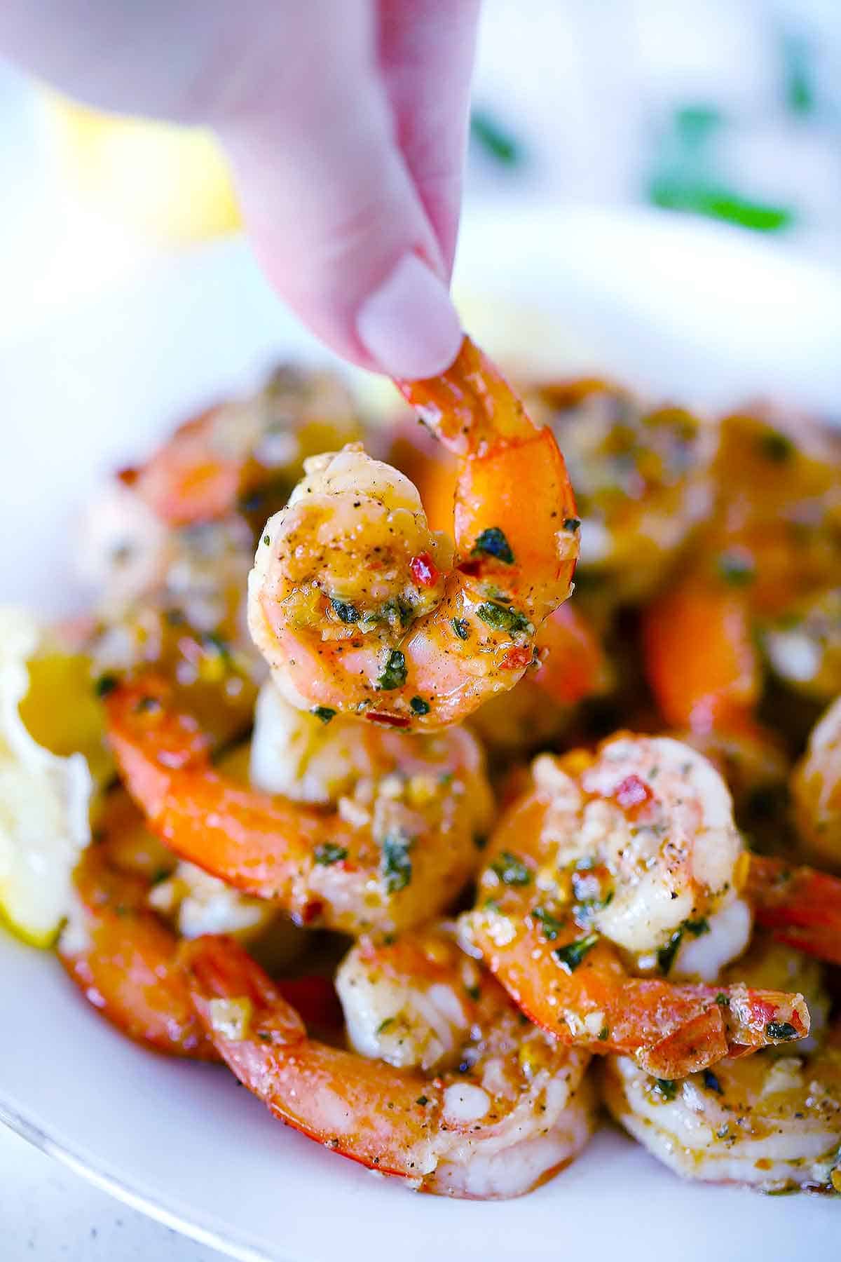 A hand holding a piece of sauteed shrimp by the tail.