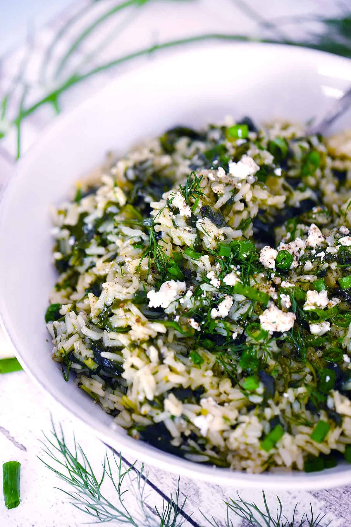 Close up photo of Spanakorizo, or Greek spinach and rice with lemon and dill, with a spoon taking a scoop and garnished with crumbled feta.