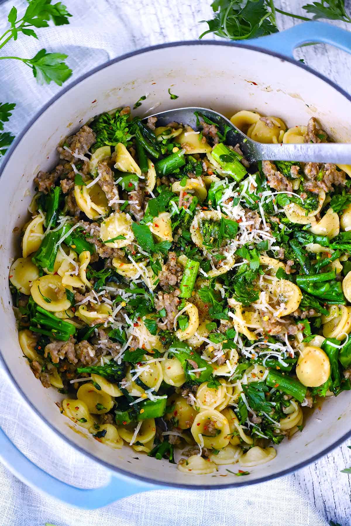 An overhead photo of a Dutch oven with orecchiette with sausage and broccolini in it.