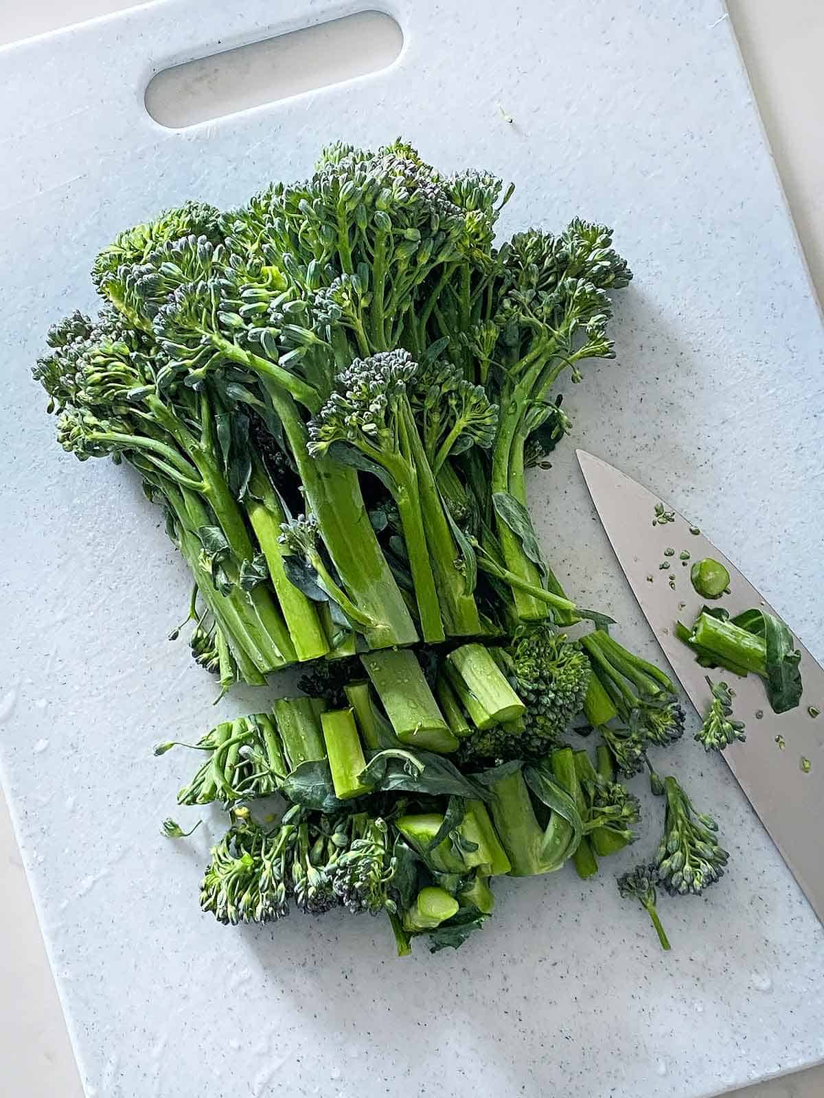 Broccolini chopped into one-half inch pieces on a cutting board.
