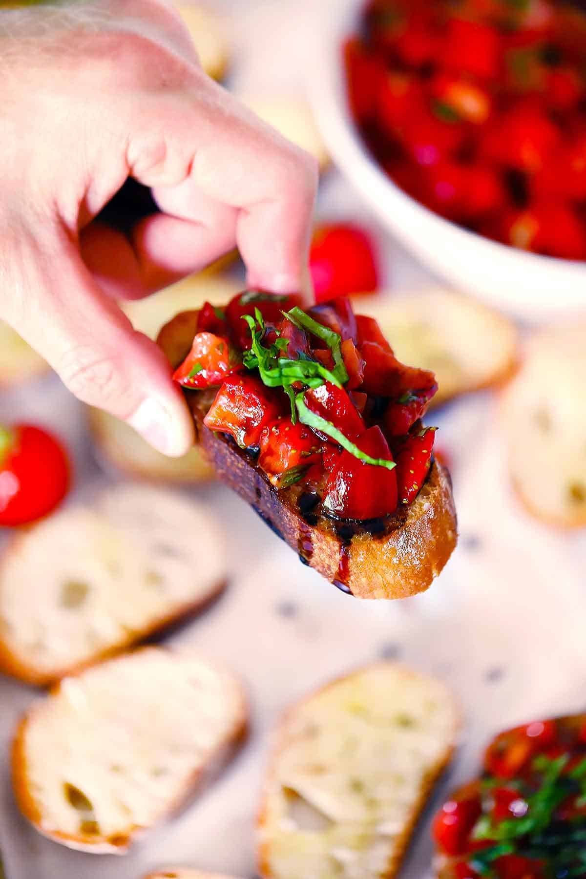 A hand holding a crostini with strawberry bruschetta on top.