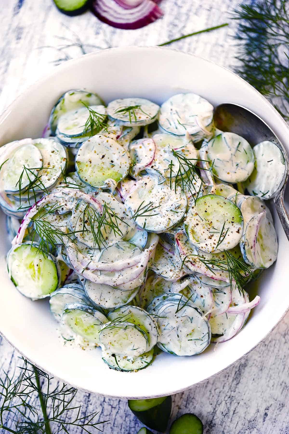 Overhead photo of a white bowl of creamy cucumber salad.