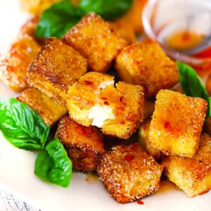 Square photo of fried halloumi bites piled up and drizzled with hot honey.