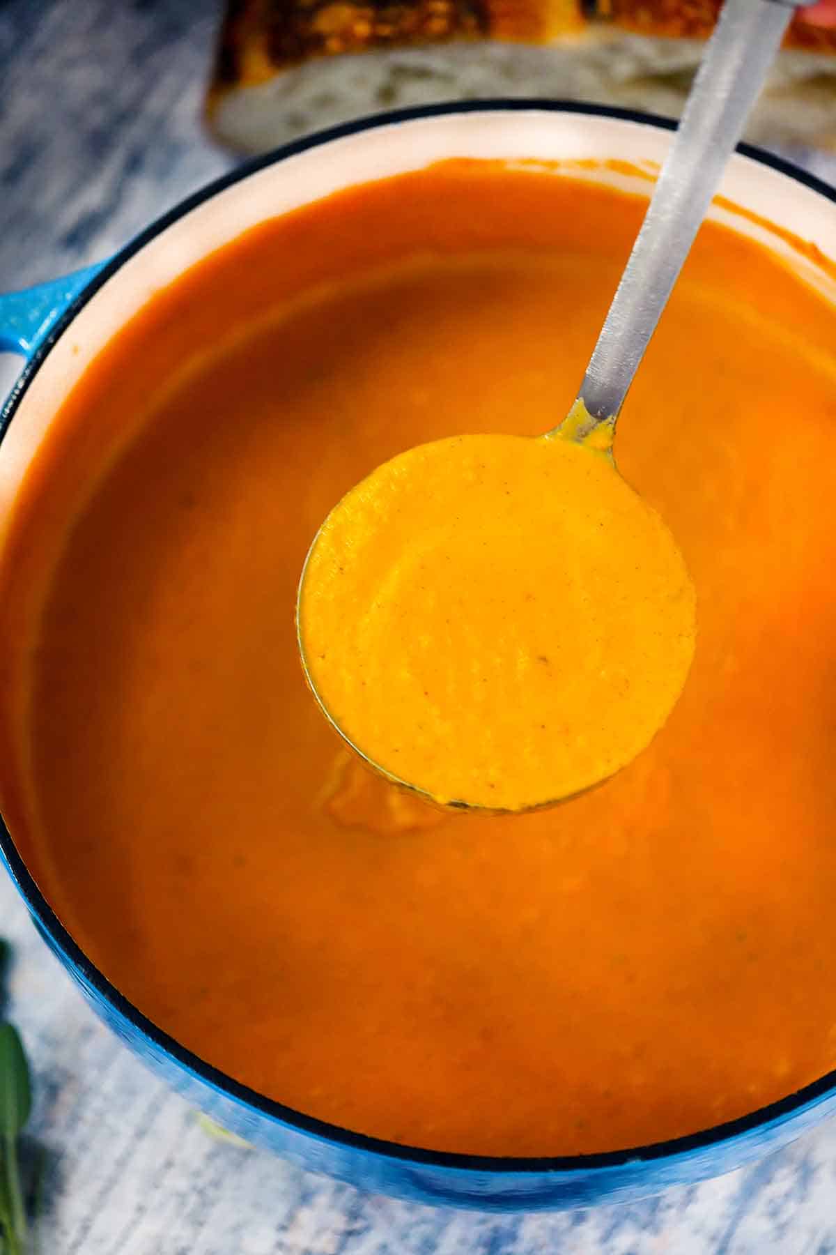 A ladle scooping out some pumpkin soup from a Dutch oven.