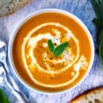 Square photo of pumpkin soup in a white bowl with sage garnish.