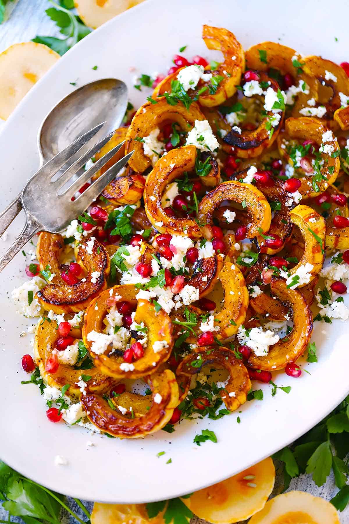 Roasted delicata squash on a white platter topped with goat cheese and pomegranate seeds.