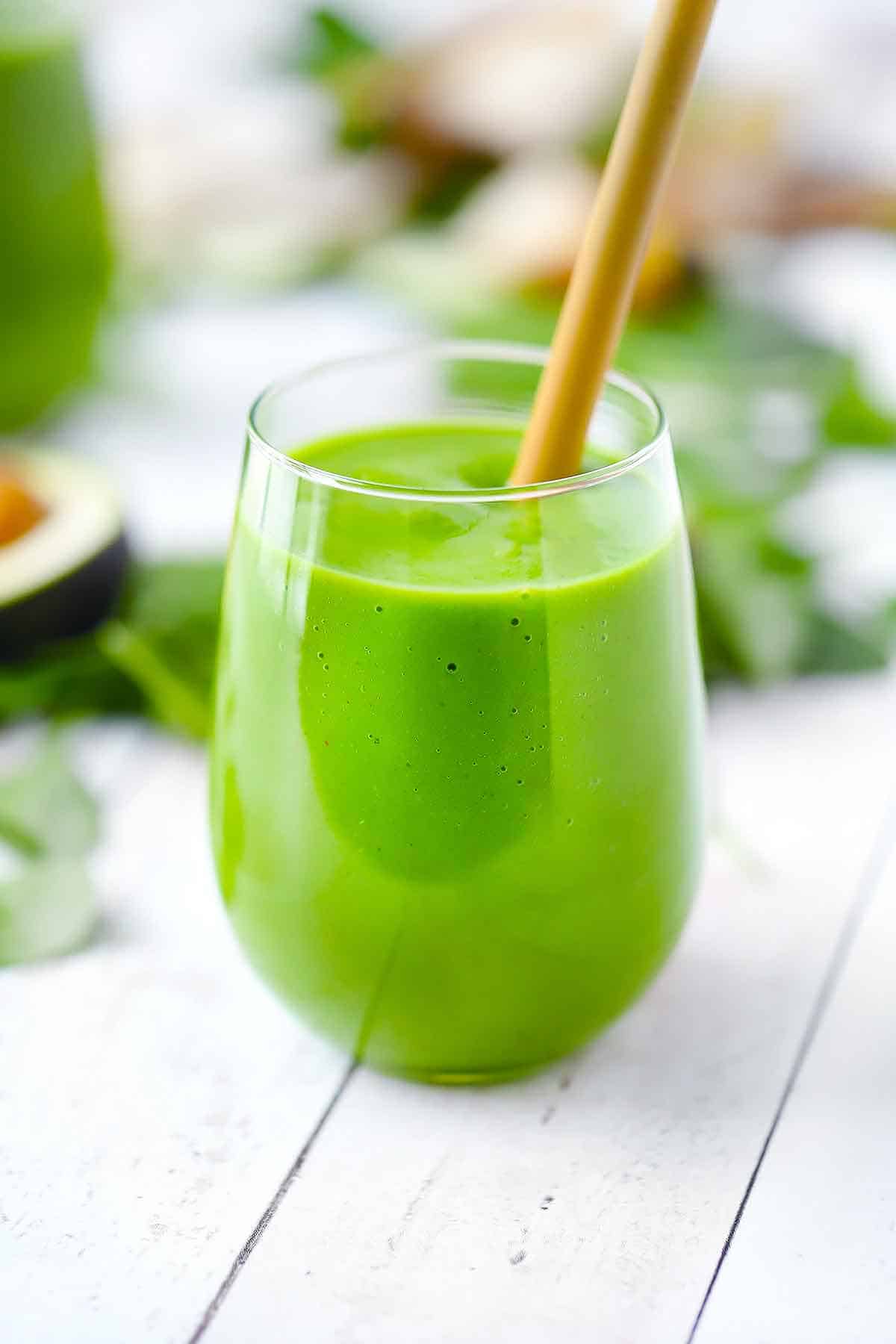 Close up photo of a green smoothie in a wine glass with a bamboo straw.