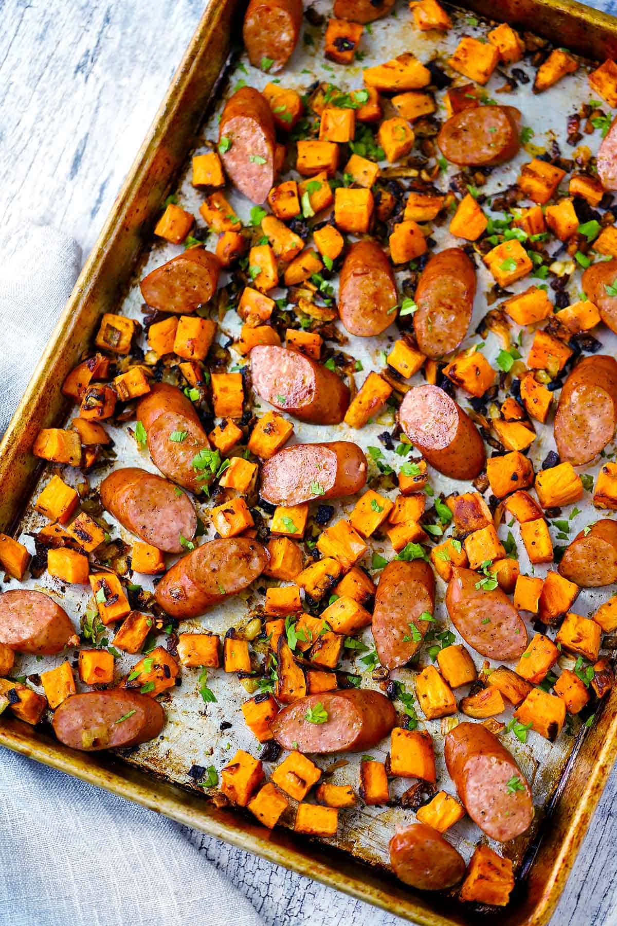 Overhead photo of a sheet pan with roasted sausage and sweet potatoes with onions and garlic.