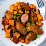 Square photo of white plate with sausage sweet potato sheet pan dinner on it.