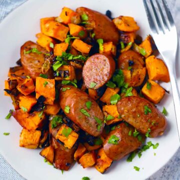 Square photo of white plate with sausage sweet potato sheet pan dinner on it.