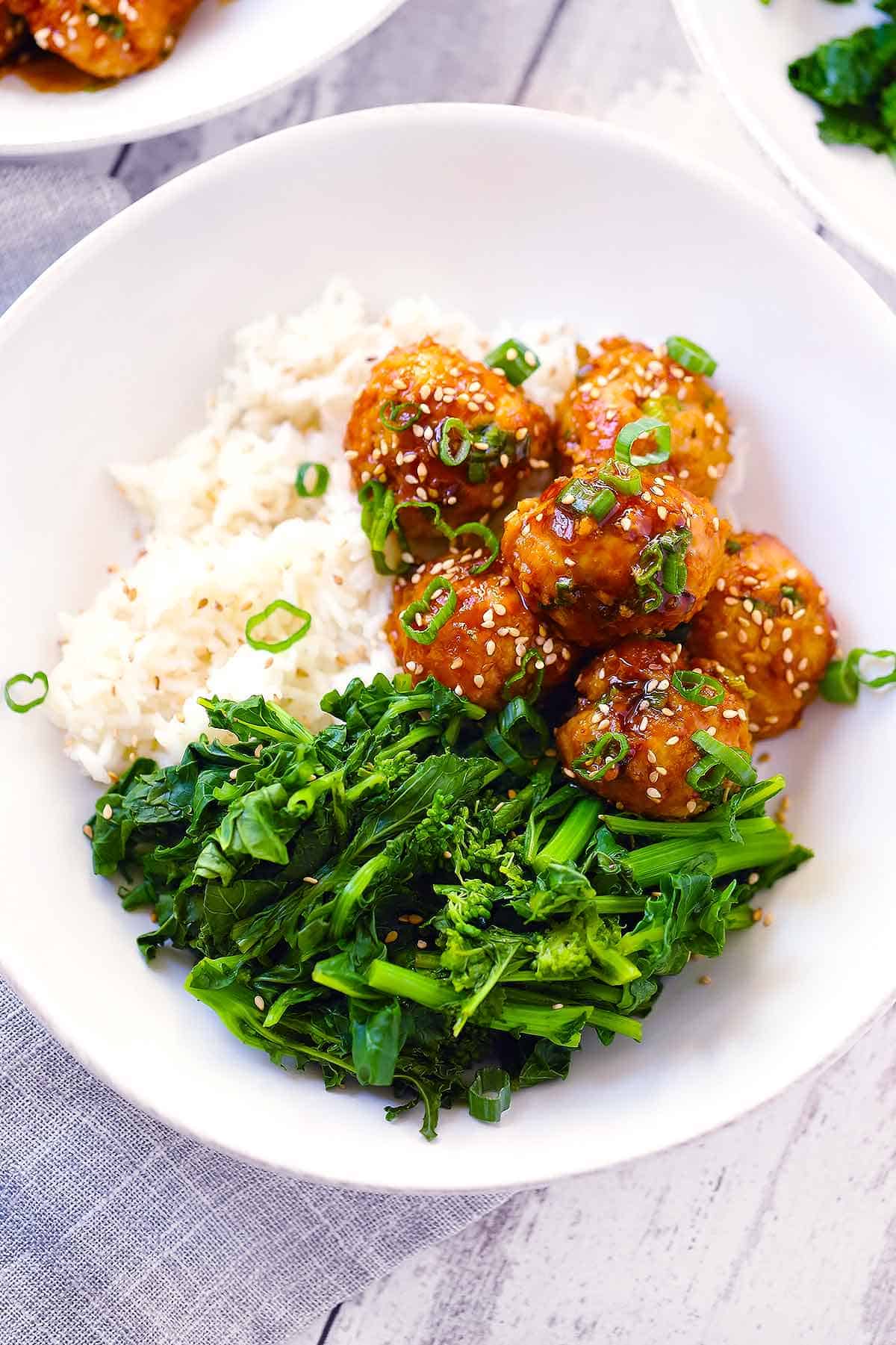 White bowl with rice, steamed Chinese broccoli, and Asian chicken meatballs.