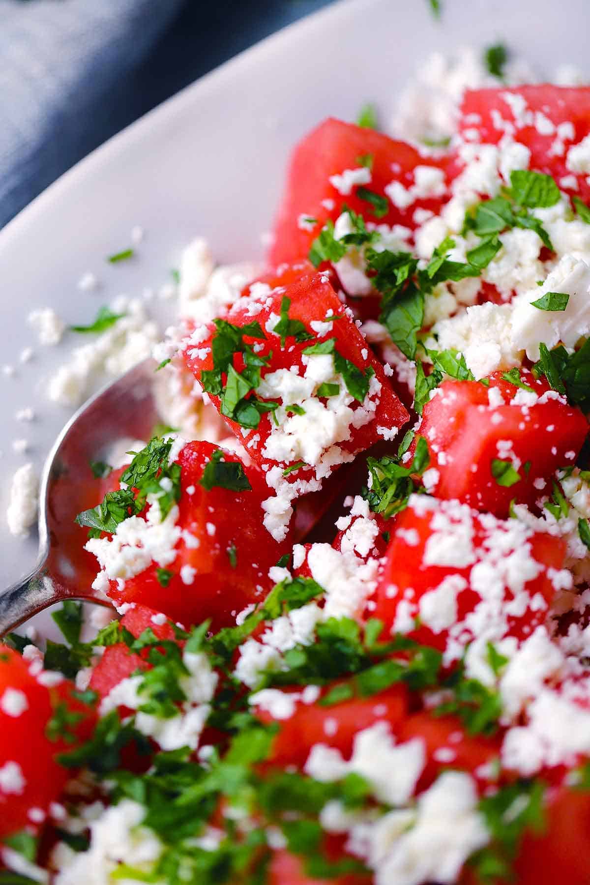 Close up of a cube of watermelon with feta cheese and mint.