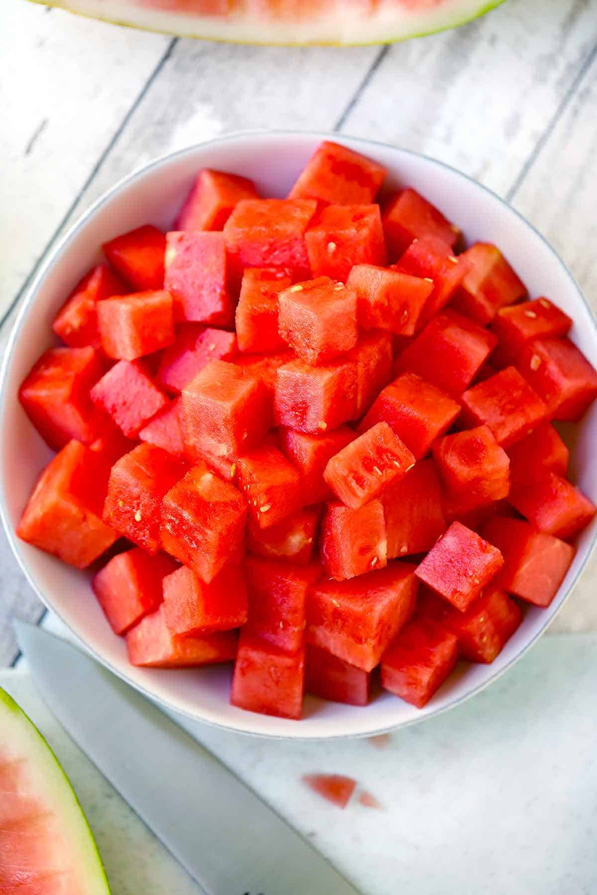 Square photo oA white bowl filled with cubed watermelon pieces.f cubed watermelon in a white bowl.