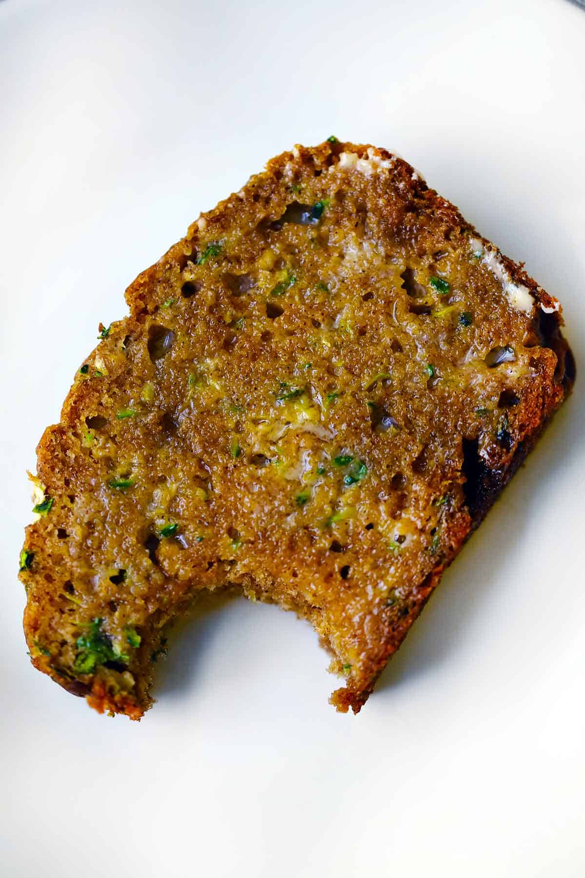 A buttered piece of zucchini bread with a bite taken out showing the texture.