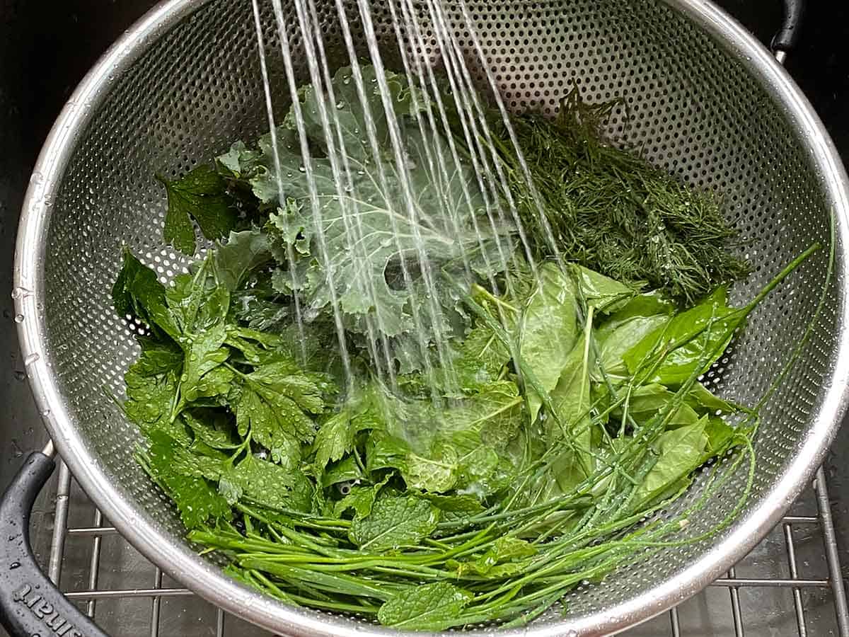 Washing off herbs and kale in a colander for Green Goddess Dressing.
