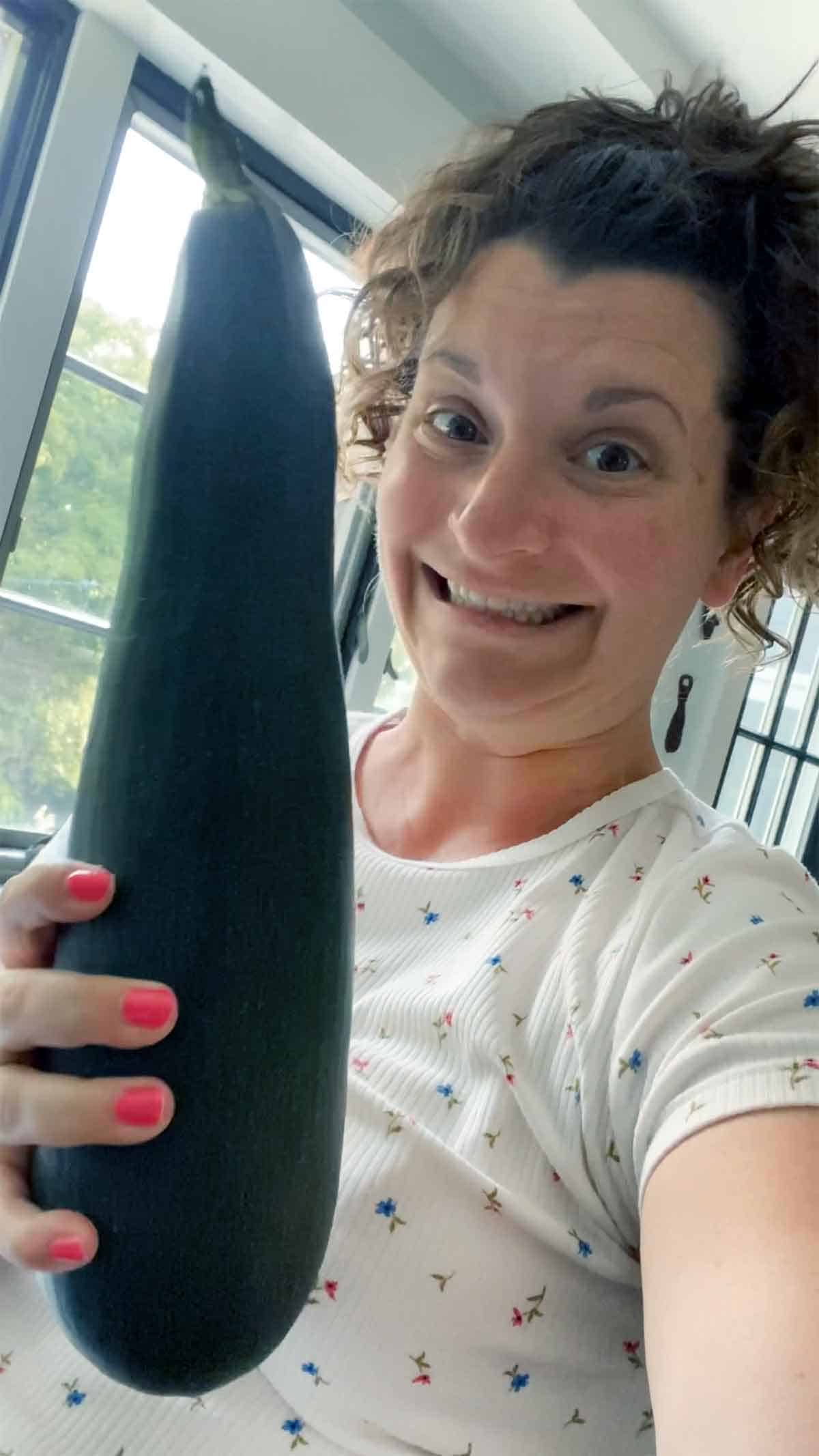 A woman holding a zucchini.
